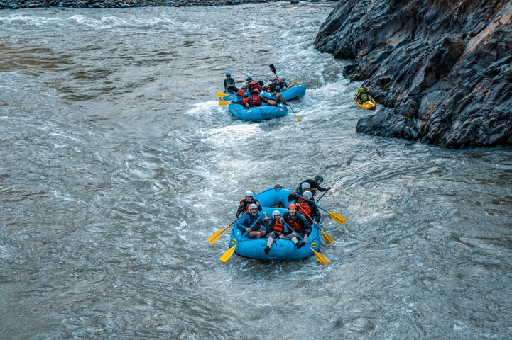       Multiple rafts with people paddling on a river.
  