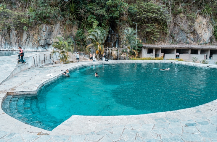       People swimming in a beautiful pool with waterfall.
  