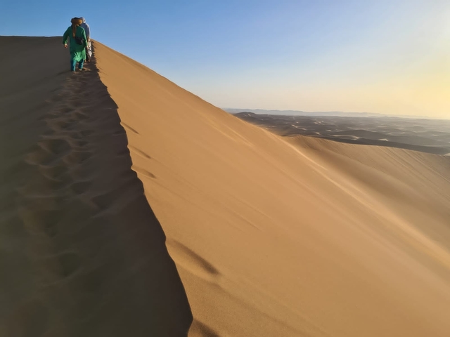      People walking on a sand dune.
  