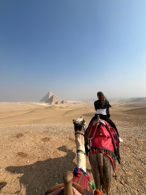 Person on a camel looking at the pyramids in a desert landscape.