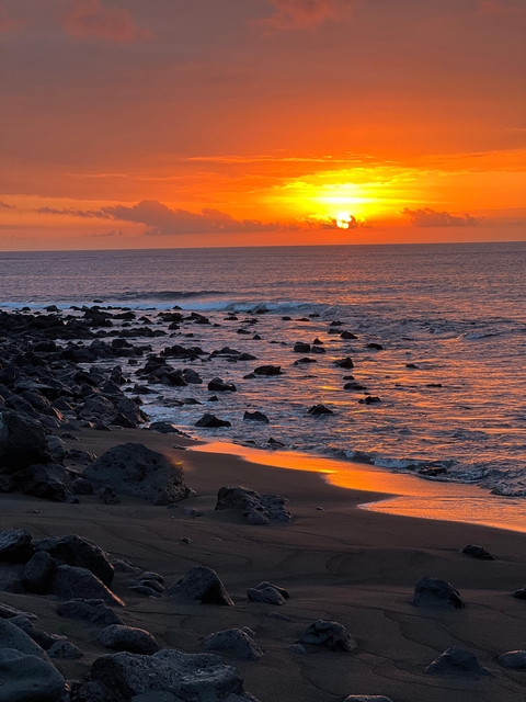 Rocky shoreline with waves and a sunset over the ocean.
