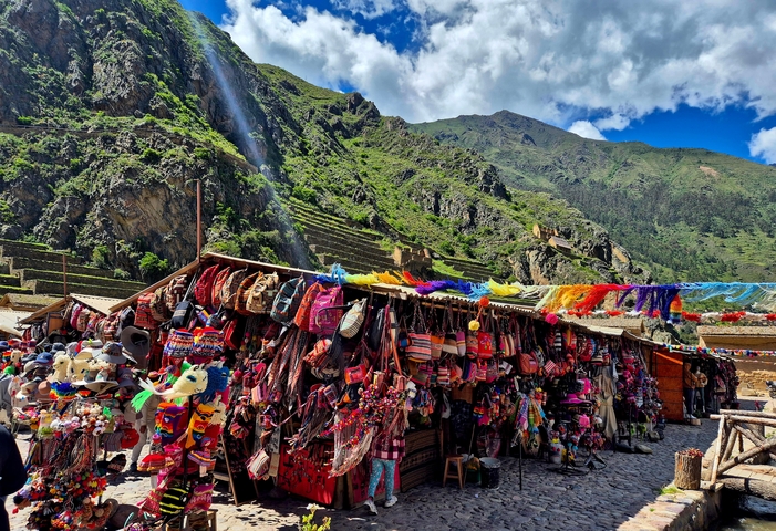 Open-air market with various colorful textiles against a mountain backdrop.