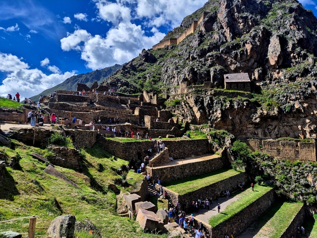 Ancient terraced ruins with visitors, set against dramatic mountain landscape.