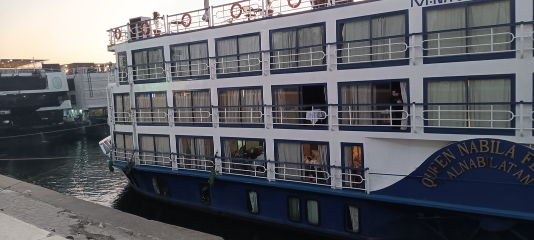       Cruise ship docked at a riverport with people onboard.
  