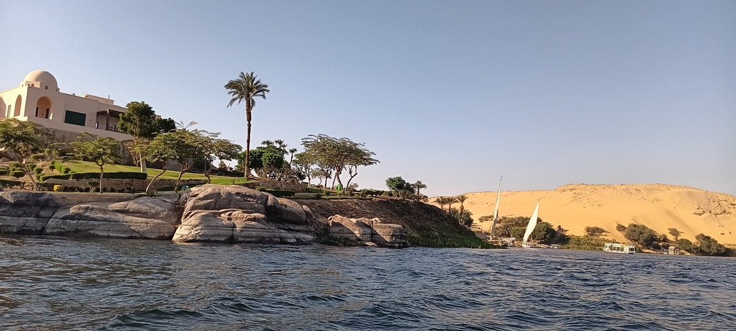       Scenic river view with rocks, trees, and a distant boat.
  