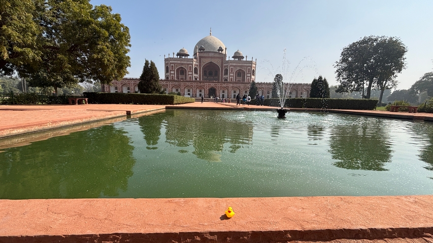      Tourists taking a photo in front of a historic mausoleum with a garden and water feature in New Delhi.
  