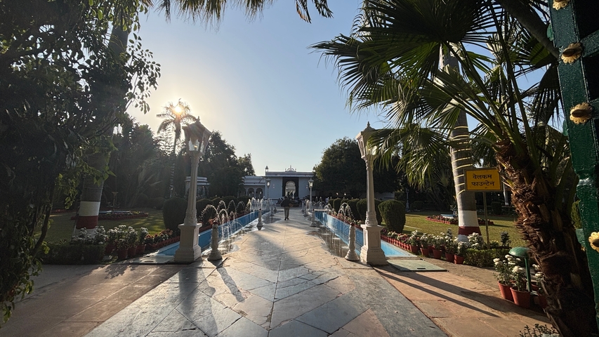       A scenic pathway leading to a historic site with palm trees and blooming flowers on either side.
  