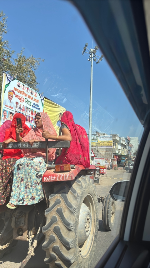       Women in traditional attire riding in the back of a vehicle on a busy street.
  