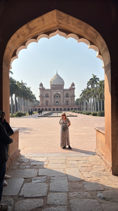       A tourist posing in front of a large mausoleum with clear skies in the background.
  