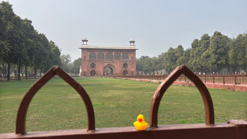       A rubber duck on a fence in front of a historic fort.
  