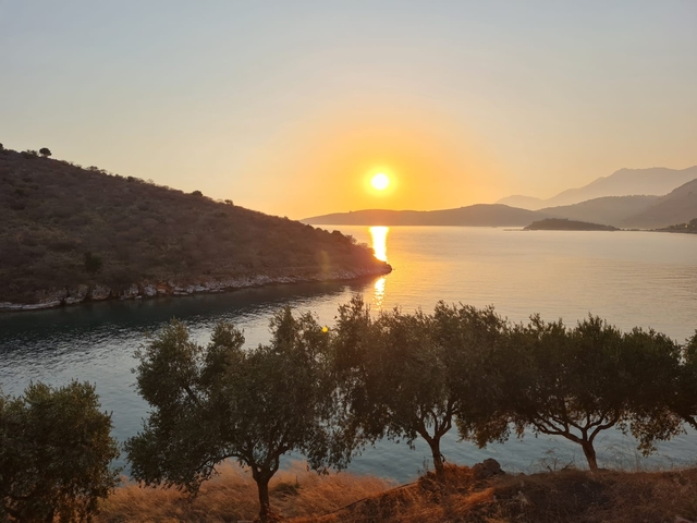 Sunset over a calm sea with distant hills.