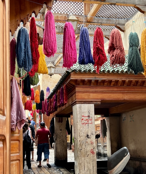       Colorful yarns hanging in a traditional market setting.
  