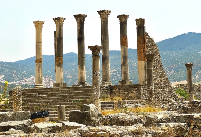       Ancient ruins with columns against a mountainous backdrop.
  