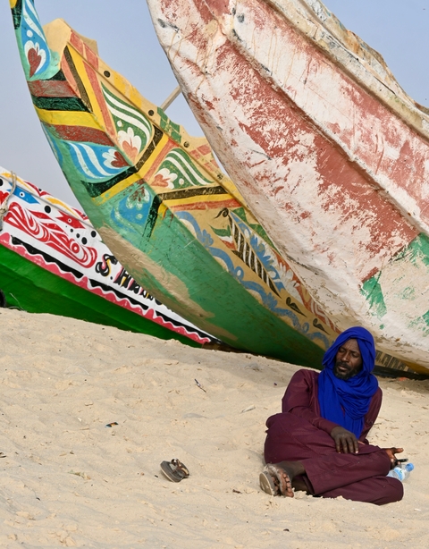 Man sitting next to brightly painted boats