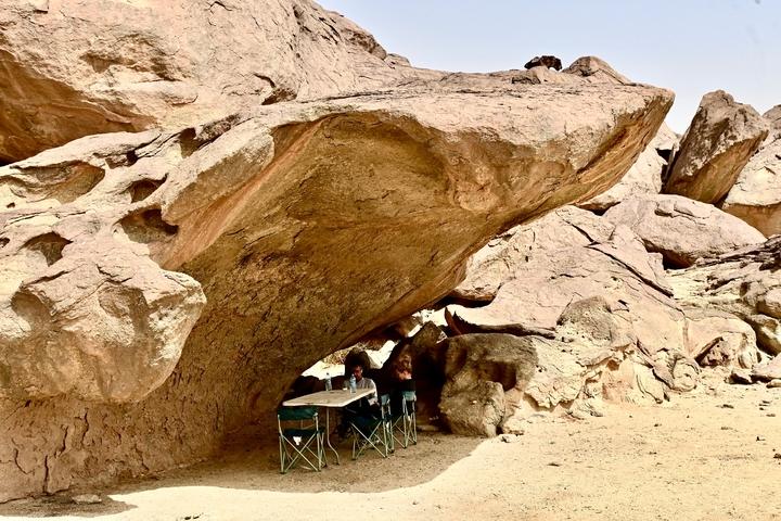 Person sitting under a large rock formation