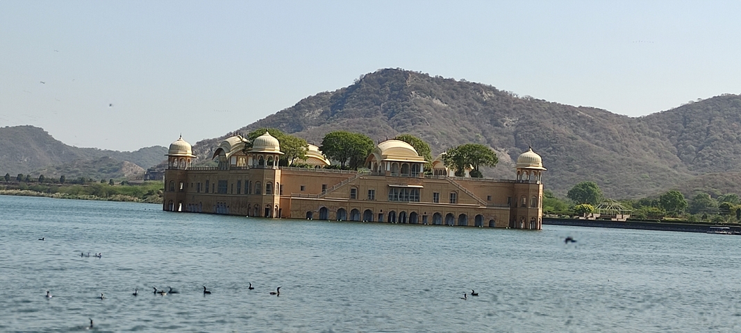 Jal Mahal, a palace in the middle of a lake with hills in the background.