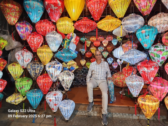 A man sitting surrounded by colorful lanterns.