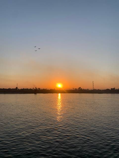 Sunset over the Nile River with birds in flight.