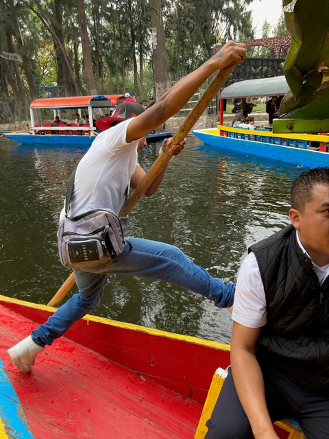       Boatman navigating a canal with decorative boats.
  