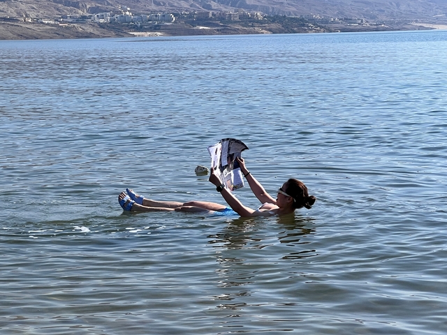 Person floating in water reading a newspaper.