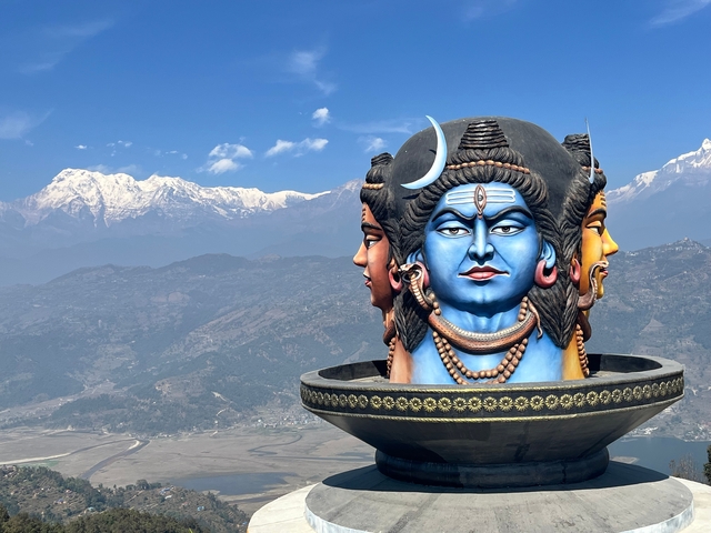 Three-faced Shiva statue with mountains in the background.