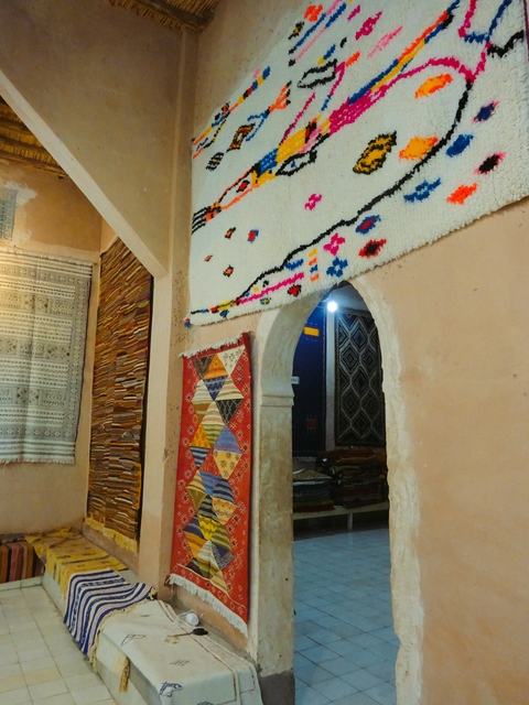       Interior of a Moroccan shop with colorful woven carpets and textiles.
  