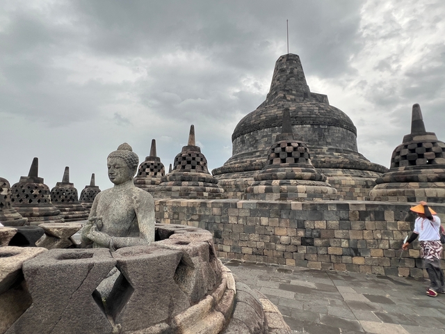 Statues and stupas at Borobudur with a person in traditional attire.