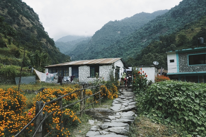       Stone house with a garden and mountains in the background.
  