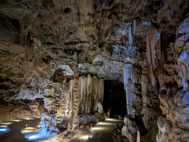 Cavern with stalactites and stalagmites illuminated by artificial lights.