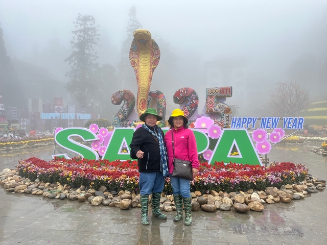       Two people standing in front of Sapa sign with fog and floral decorations.
  