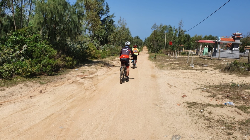       Cyclists riding on a dirt path surrounded by trees and vegetation.
  