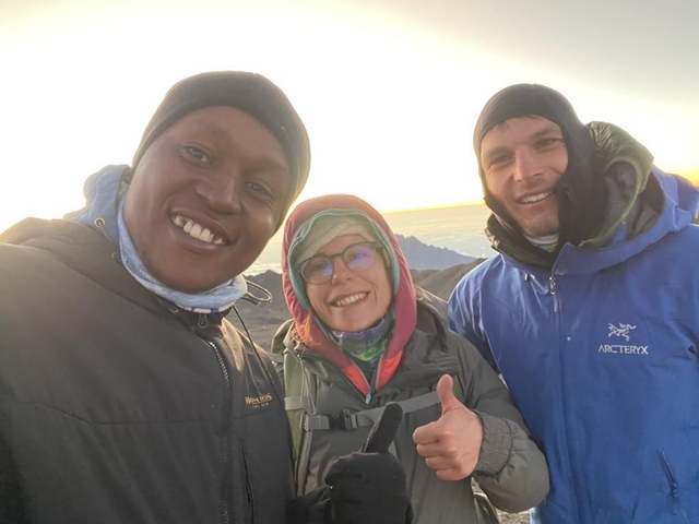 Three people smiling with a scenic mountain view at sunset.