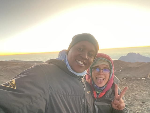 Two people posing with a scenic mountain view at sunset.