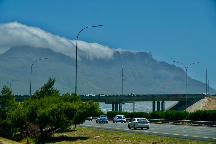A busy highway with cars and a mountain in the background partially covered by clouds.