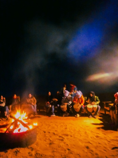       A group of people enjoying a night gathering with drums and fire.
  