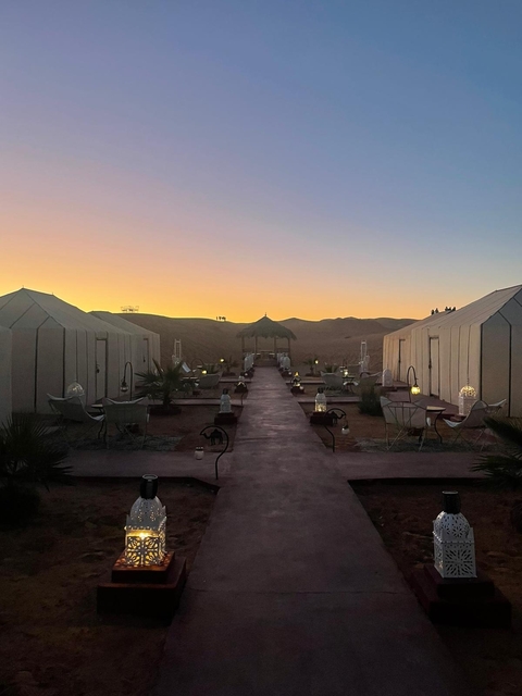       A desert camp at sunset with tents and lanterns.
  
