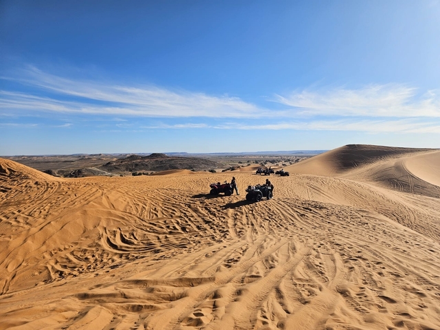       Groups of people driving ATVs up sand dunes in a desert landscape.
  