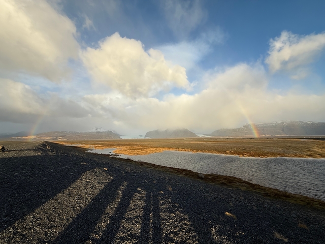 A scenic landscape with a rainbow over water and mountains.