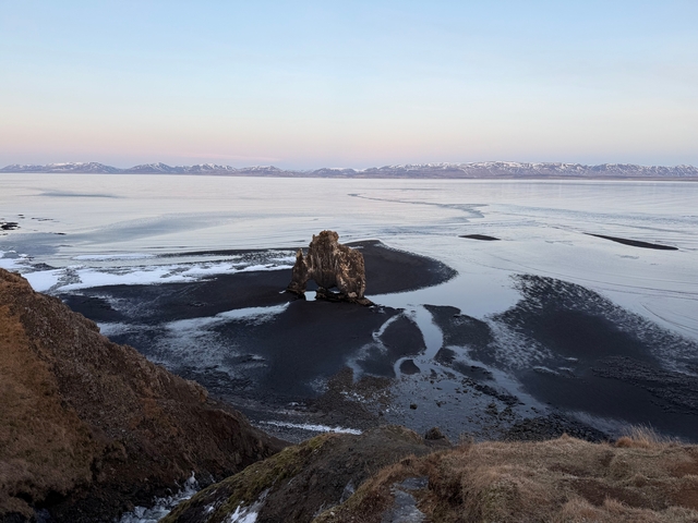 A natural rock formation in a vast landscape with snowy mountains.