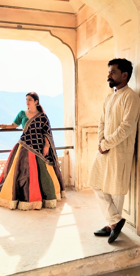 Man and woman in traditional attire posing in front of a scenic view.