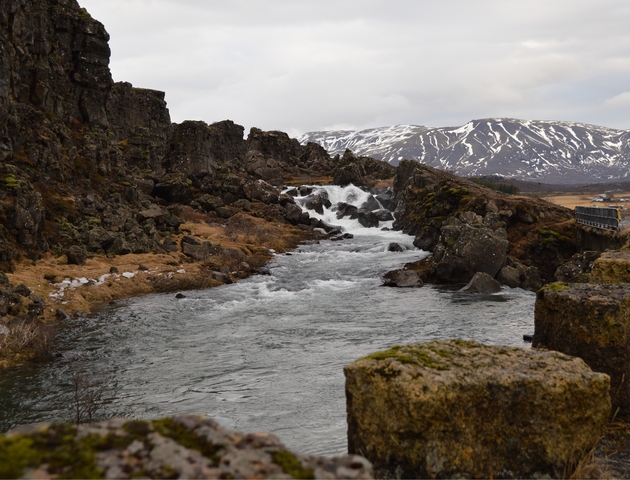       River flowing through rocky landscape with snow-capped mountains.
  