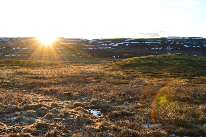       Sun rising over an open field with snow patches.
  