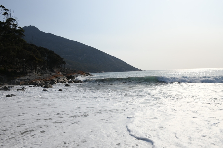       Waves crashing on a rocky shore with a mountain in the background.
  