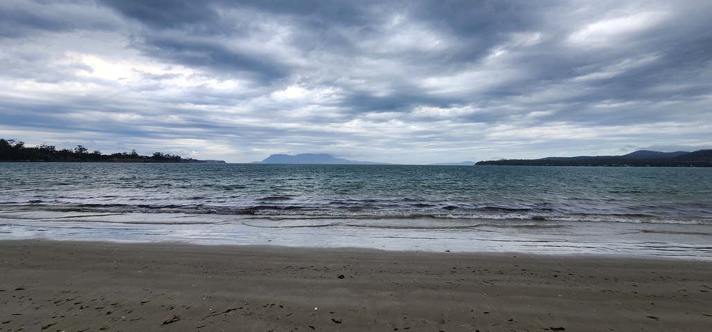       Cloudy sky above a calm sea viewed from a sandy beach.
  