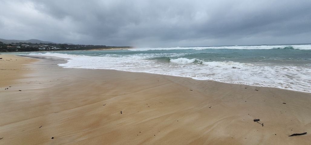       Sandy beach with waves under a cloudy sky.
  