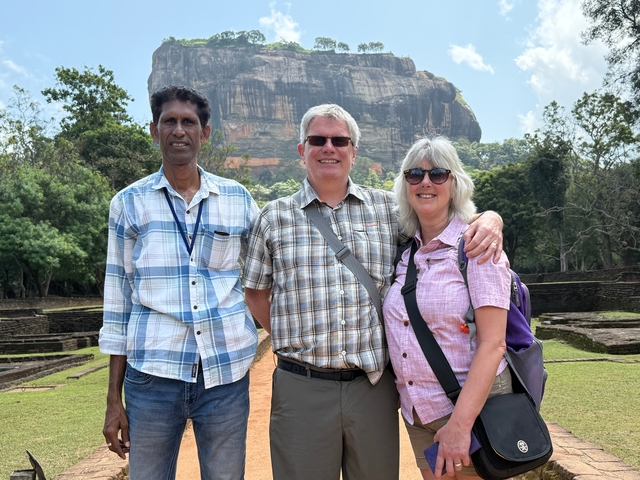       Three people posing in front of the rock fortress with greenery.
  