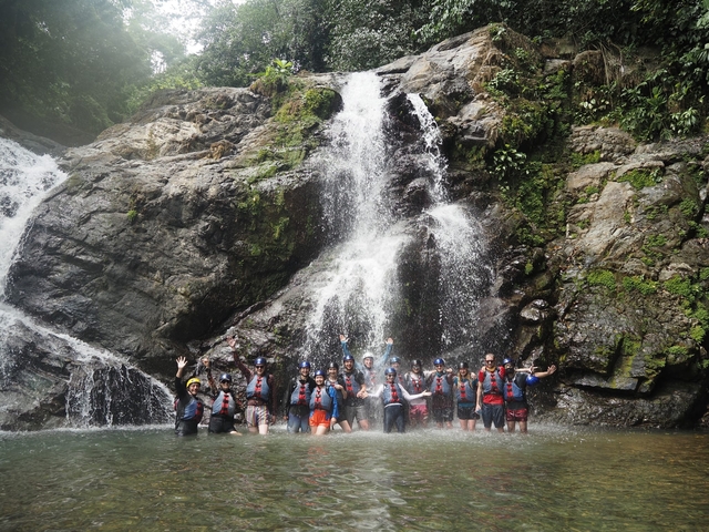 People enjoying a waterfall dressed in life jackets and helmets.