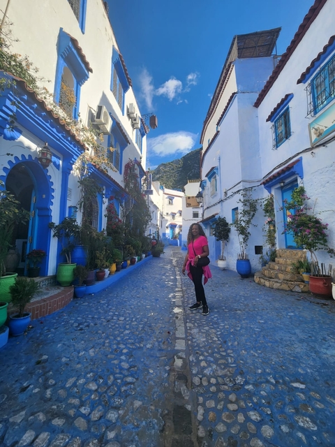       Street view with blue buildings and a woman in a bright pink outfit.
  