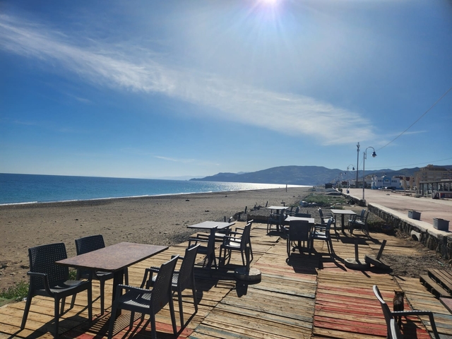 Empty beachside cafe with tables and chairs, overlooking the sea.