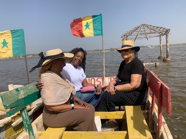       Women sitting on colorful chairs on a boat by a lake.
  